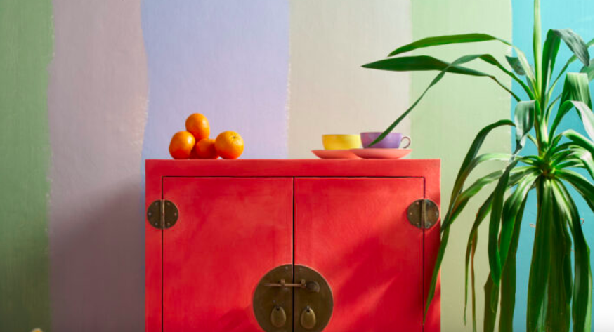 Red painted cabinet against a multicoloured wall with a leafy plant